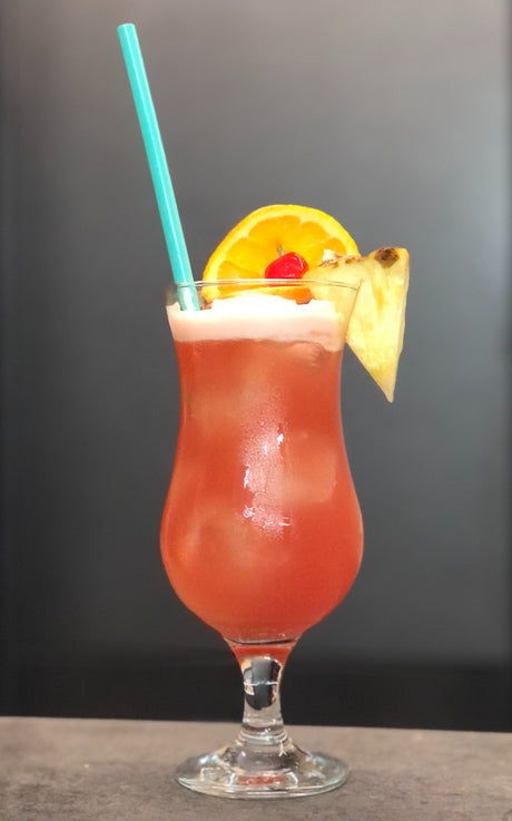Planter’s Punch Cocktail mit Eis, Orangenscheibe, Cocktailkirsche, Ananasstück und türkisfarbenem Trinkhalm im Hurricaneglas.