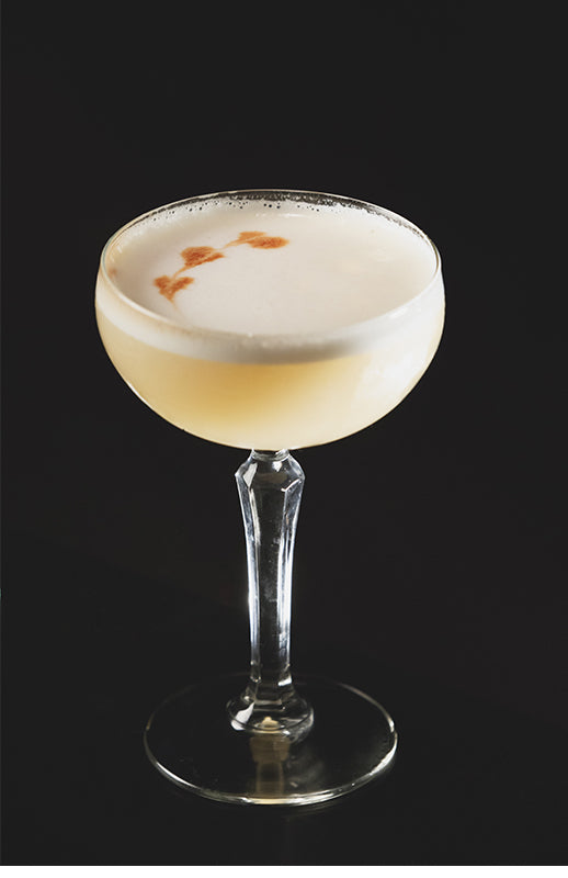 Spicy Pisco Sour im Coupette-Glas mit heller Schaumkrone und Bitters-Dekoration auf schwarzem Hintergrund.