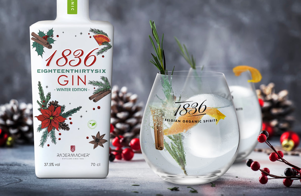 1836 Gin Winteredition neben Servierglas mit Tonic, Eis, Orangenzeste und Rosmarin, umgeben von winterlicher Dekoration und Zapfen.