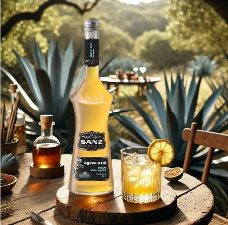 Blaue Agavensirup Sanz 0,7L auf rustikalem Holztisch mit Cocktail und Agavenpflanzen im Hintergrund