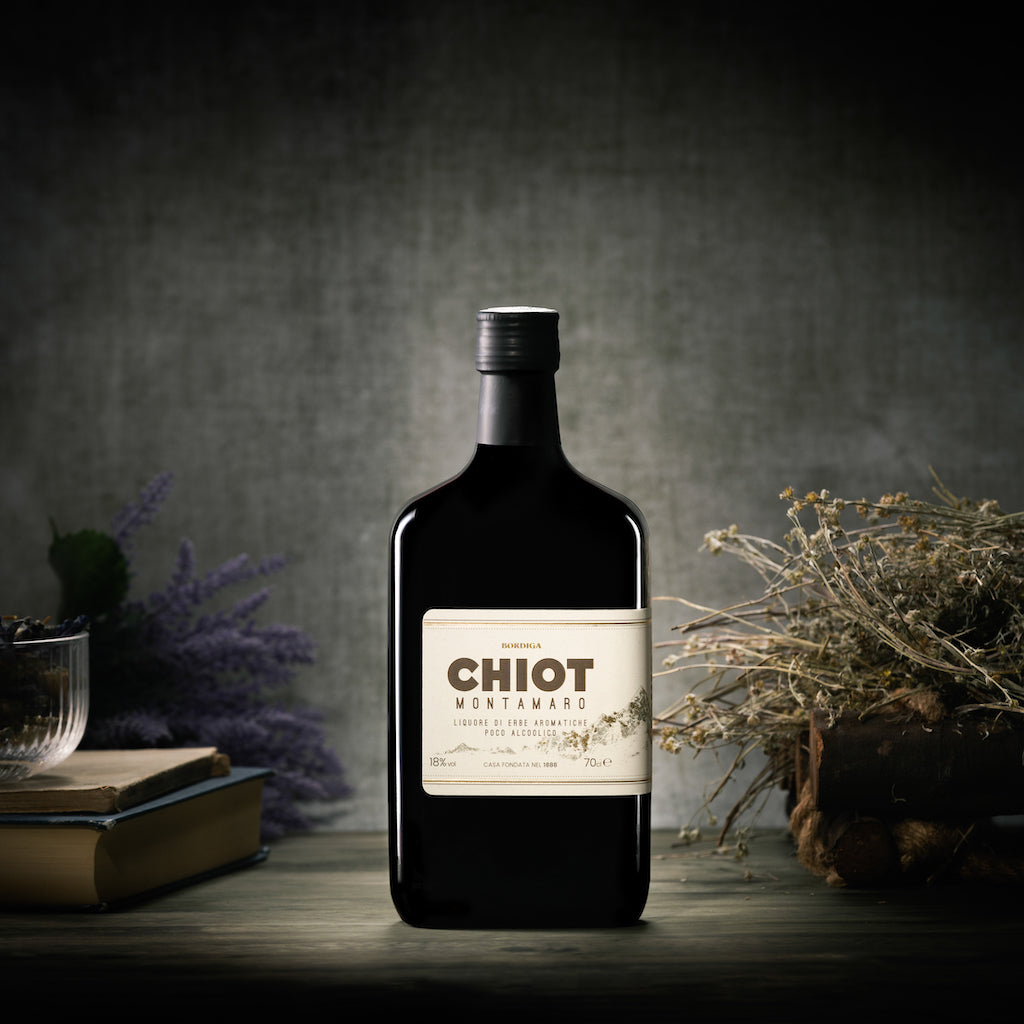 Flasche Chiot Montamaro Kräuterlikör von Bordiga, arrangiert mit getrockneten Kräutern und Lavendel vor rustikalem Hintergrund.