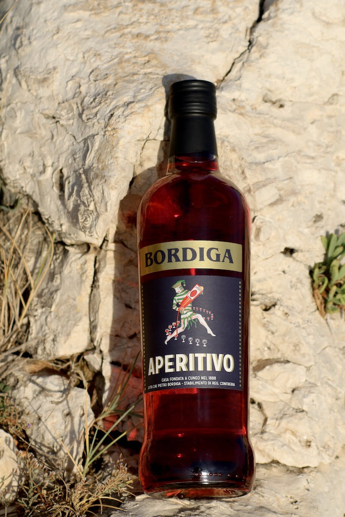 Flasche Bordiga Aperitivo auf hellem Felsen, umgeben von trockenem Gras und mediterraner Vegetation bei Sonnenlicht.