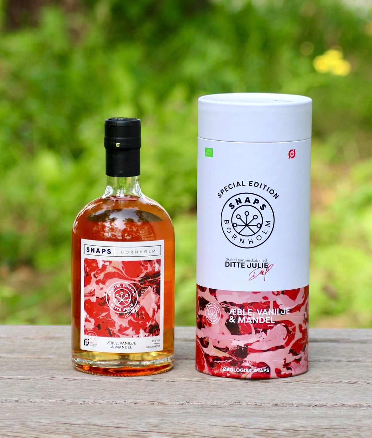 Flasche und Geschenkbox Bio-Schnaps von Bornholm, Apfel, Vanille, Mandel, auf Holzoberfläche vor unscharfem, grünem Hintergrund.