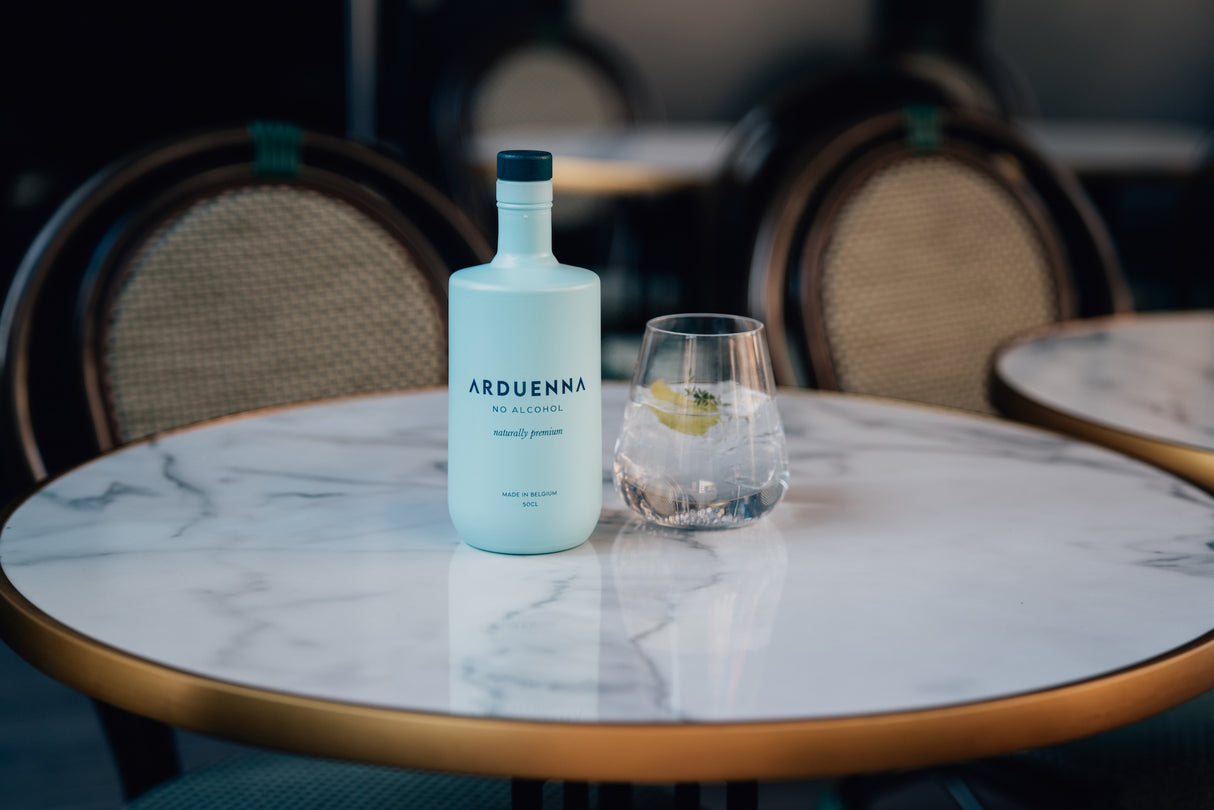 Arduenna No Alcohol 0,5 l mit Glas Tonic, Eis, Zitrone und Thymian auf rundem Marmortisch mit Bistrostuhl im Hintergrund