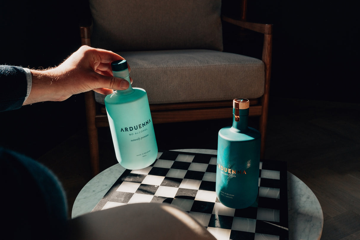 Arduenna No Alcohol 0,5 l in Hand vor Arduenna Organic Gin auf Schachbrett-Tisch in moderner Sitzecke