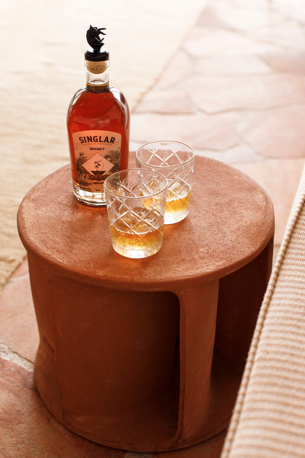 Singlar Whisky 8 Jahre mit zwei gefüllten Gläsern auf einem runden Tisch, Innenaufnahme in warmer Atmosphäre.