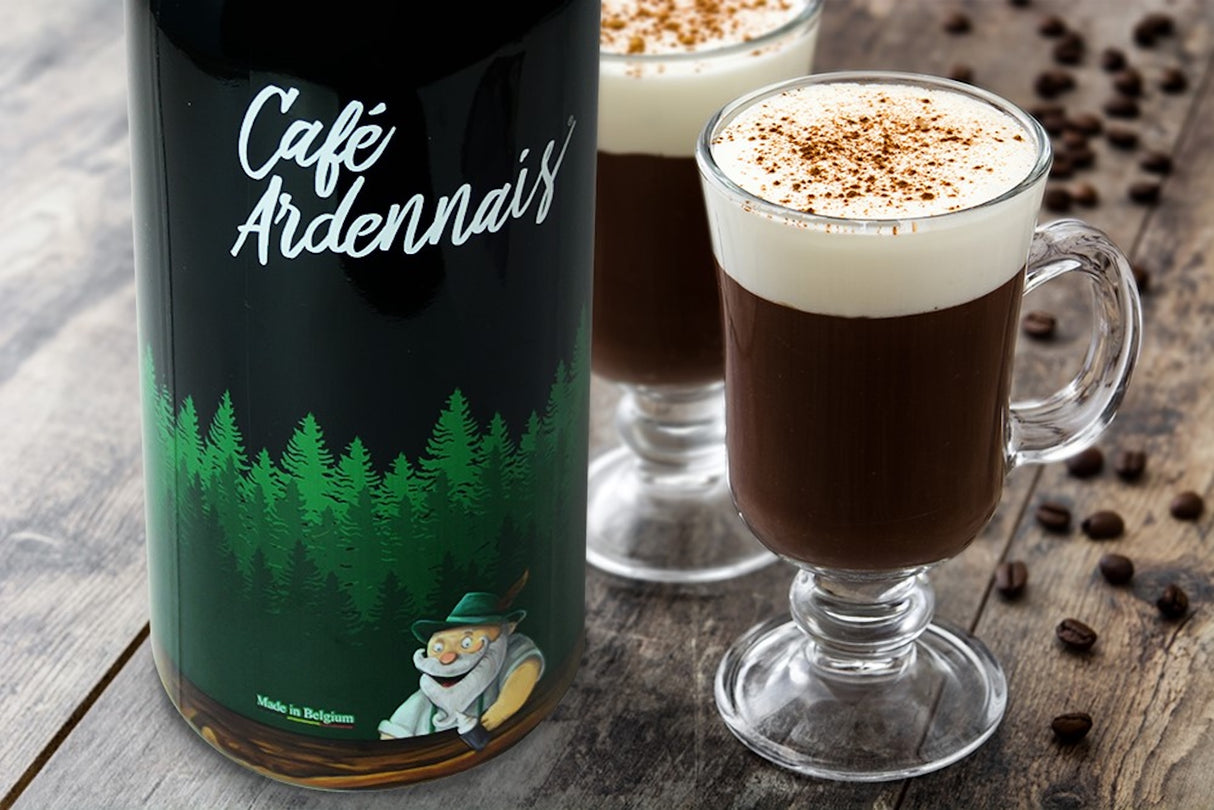 Flasche Café Ardennais Kaffeelikör neben zwei Gläsern mit Kaffeelikör, Sahne und Zimt auf Holz.