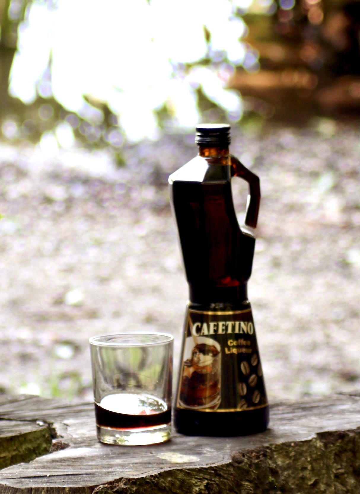 Cafetino Kaffeelikör in Kaffeekocher Flasche mit Glas auf Holz vor hellem Naturhintergrund
