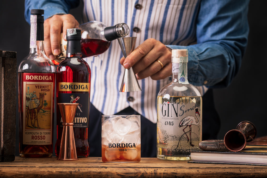 Bartender misst Aperitif ab, davor ein Cocktailglas mit Eis und Flaschen von Bordiga: Vermouth Rosso, Aperitivo und Ciais Gin Smoke.