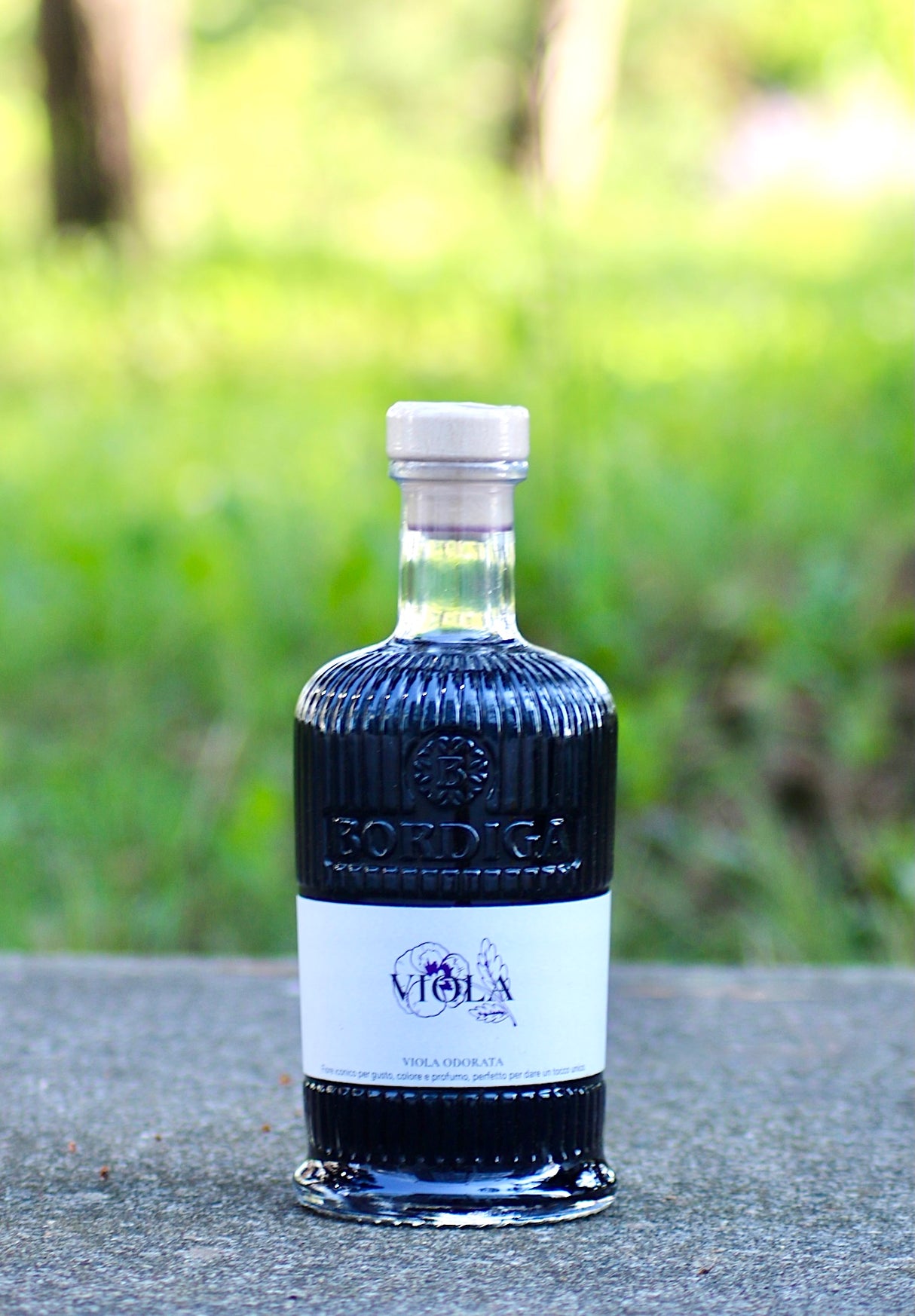 Bordiga Elisir Viola Likör 700 ml auf grauer Fläche vor unscharfem grünen Hintergrund