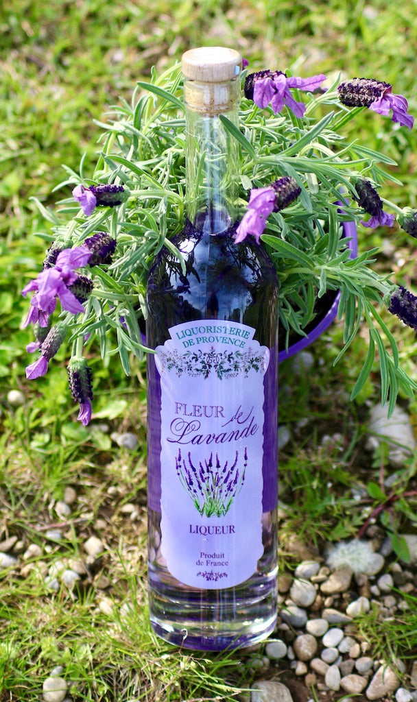 Flasche Fleur de Lavande Likör umgeben von frischen Lavendelblüten im Freien auf Kies und Gras