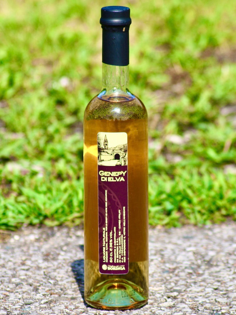 Alttext: Genepy di Elva Likör von Bordiga mit violettem Etikett, im Vordergrund und Hintergrund grüne Wiese.