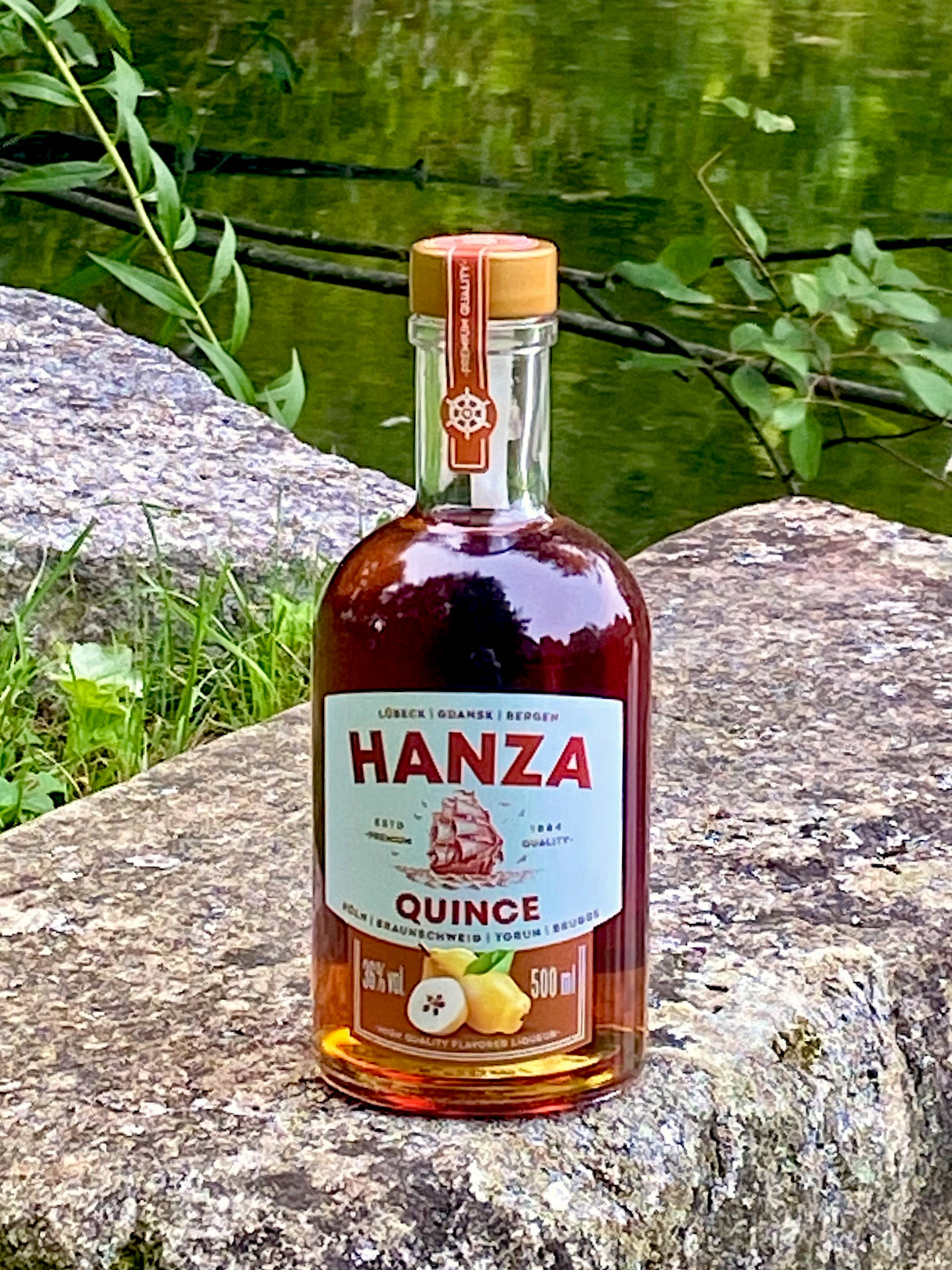 Hanza Quince Quittenlikör auf einem Felsen am See, Flasche mit Quittenmotiv und Segelschiff auf dem Etikett.
