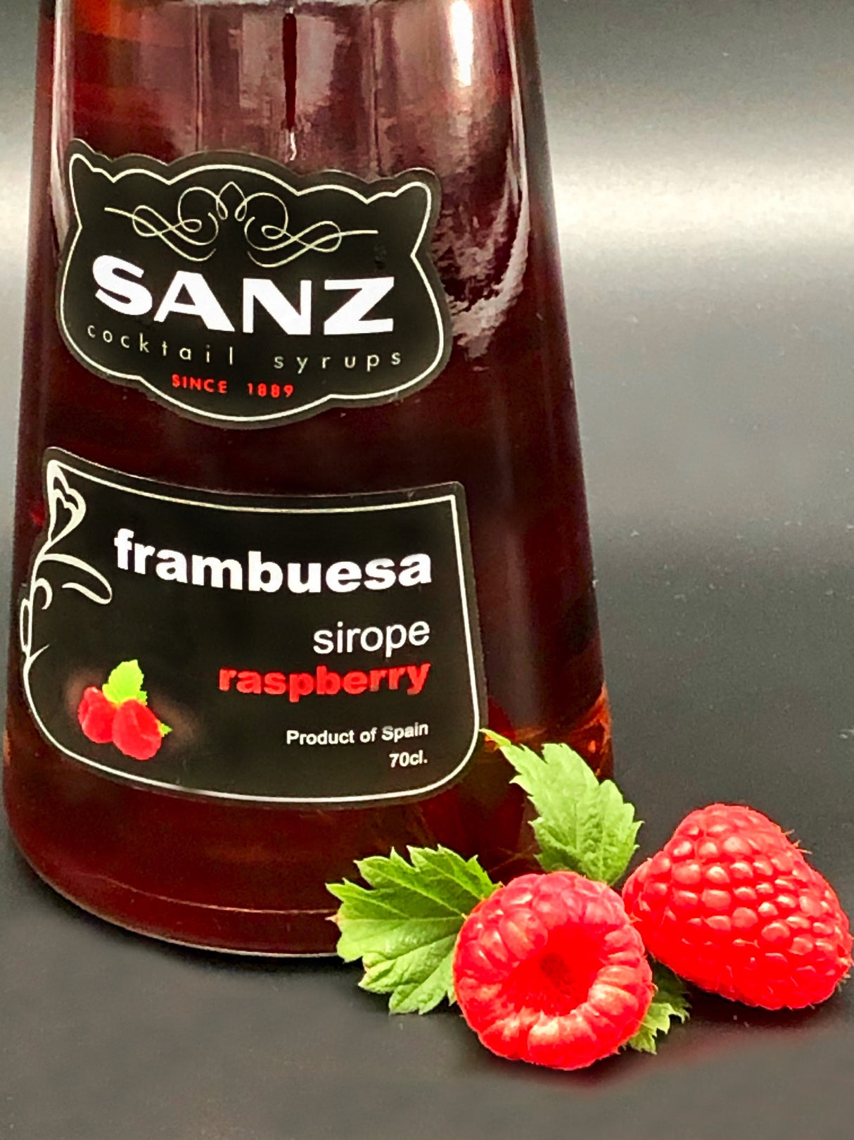 Himbeersirup Sanz 0,7L, Nahaufnahme mit frischen Himbeeren und grünem Blatt auf schwarzem Hintergrund