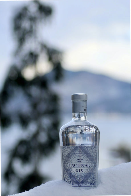 Flasche Incense London Dry Gin mit blauem Etikett, stehend im Schnee vor unscharfem Hintergrund einer winterlichen Landschaft.