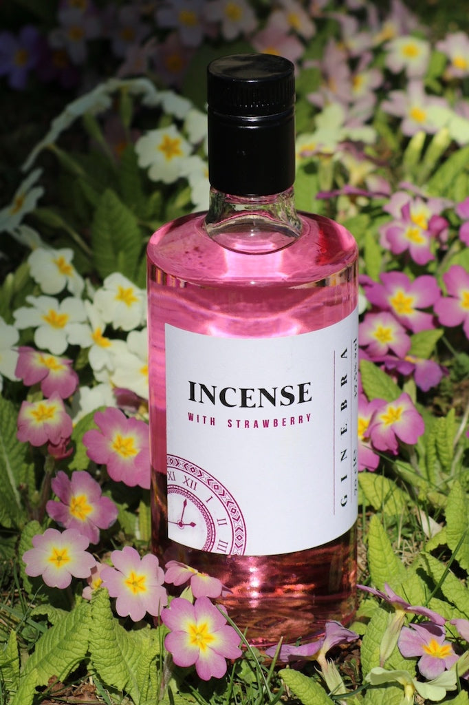 Flasche Incense Strawberry Gin umgeben von frischen Blumen in zarten Farben, präsentiert auf einer grünen Wiese.
