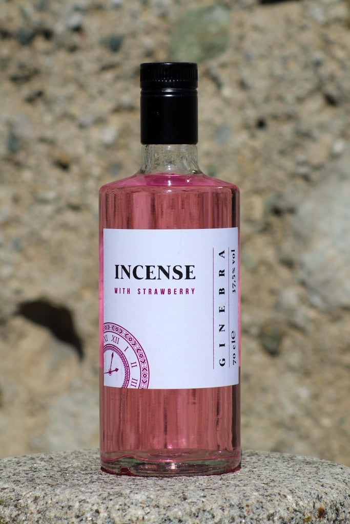 Flasche Incense Gin mit Erdbeergeschmack, rosa Flüssigkeit, stehend auf einem Stein vor unscharfem, steinigem Hintergrund.