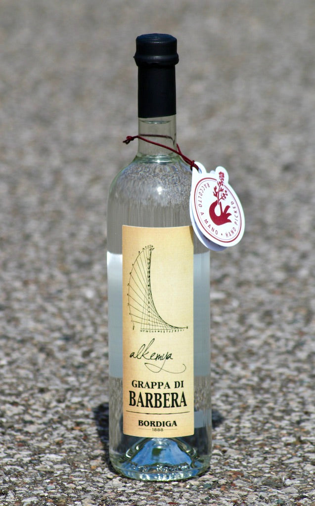 Grappa di Barbera Alkemya von Bordiga mit Anhänger, fotografiert bei Tageslicht, Etikett und Verschluss gut erkennbar.^