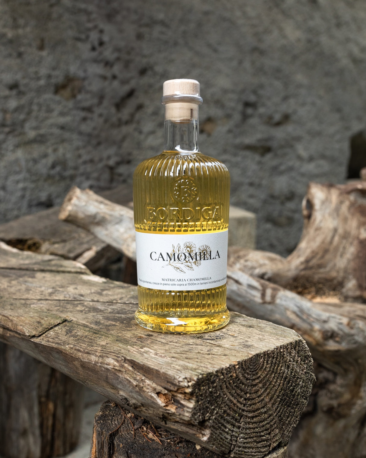 Bordiga Elisir Camomilla Kamillenlikör Flasche auf Holz vor grauem Stein- und Holzhintergrund