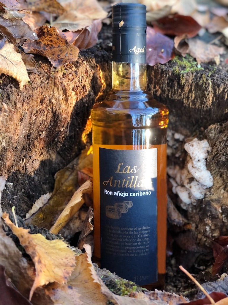 Flasche Las Antillas Ron Añejo Caribeño auf Holzfläche vor ruhigem See und unscharfem Hintergrund, 70 cl, 37,5 % Vol. Alkohol.