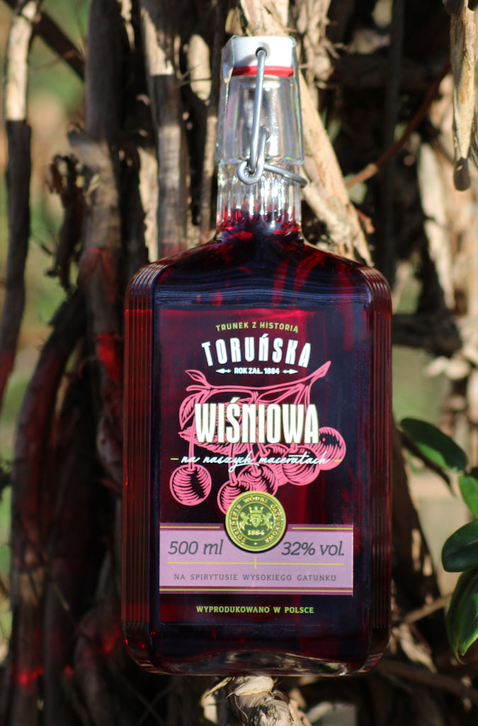 Flasche Toruńska Wiśniowa Kirschlikör, 500 ml, mit Bügelverschluss, vor rustikalem Hintergrund in natürlichem Licht präsentiert.