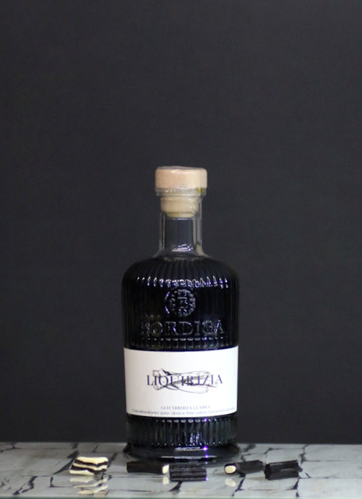 Bordiga Liquirizia Likörflasche auf Glasplatte vor schwarzem Hintergrund, dekoriert mit Lakritzstücken.