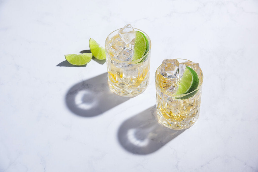 Zwei Gläser des Light & Stormy Cocktails mit Limettenscheiben und Eiswürfeln, angerichtet auf einer weißen Marmorfläche.