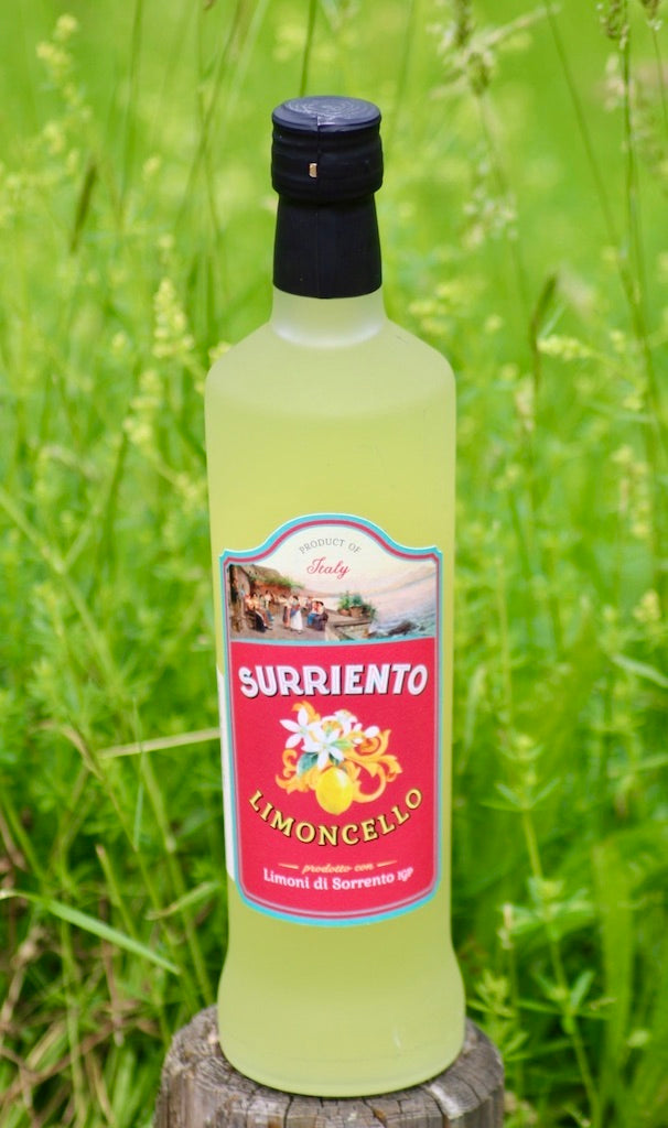 Flasche Surriento Limoncello mit rotem Etikett auf einem Holzpfosten vor grünem, unscharfem Hintergrund mit Gräsern.