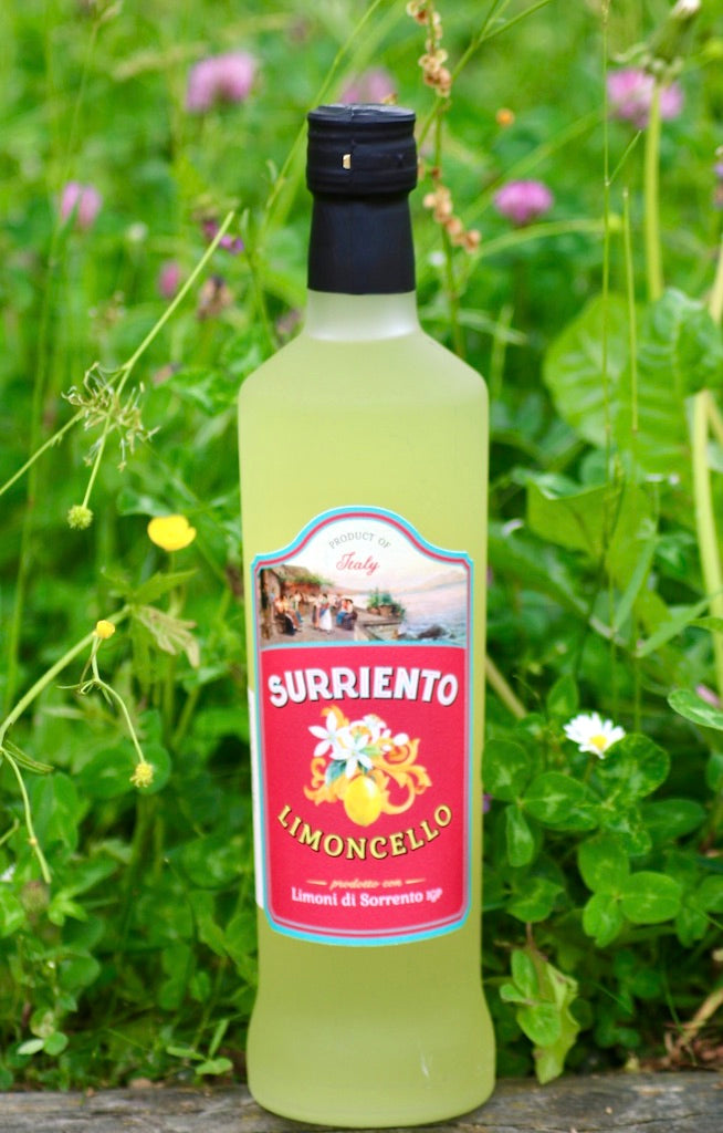 Flasche Surriento Limoncello mit rotem Etikett, stehend vor grünem Hintergrund mit Wiesenblumen und Klee.