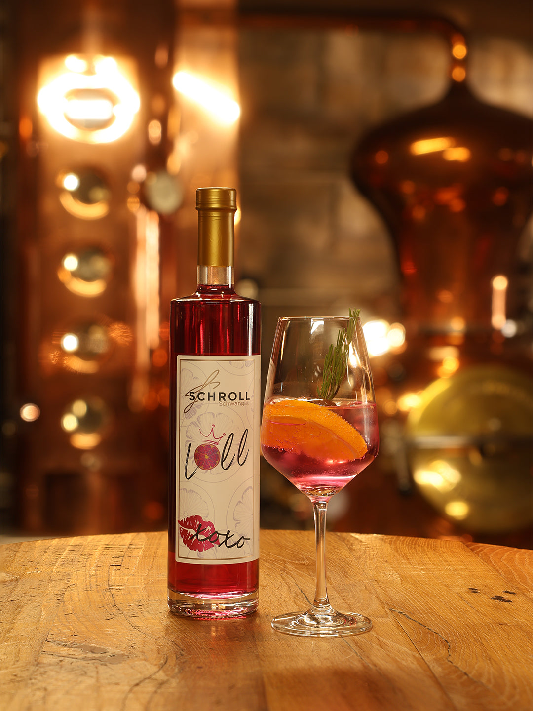 Flasche Loll Aperitif Likör und ein Glas Spritz mit Garnitur. Im Hintergrund verschwommene Kupferbrennblasen.