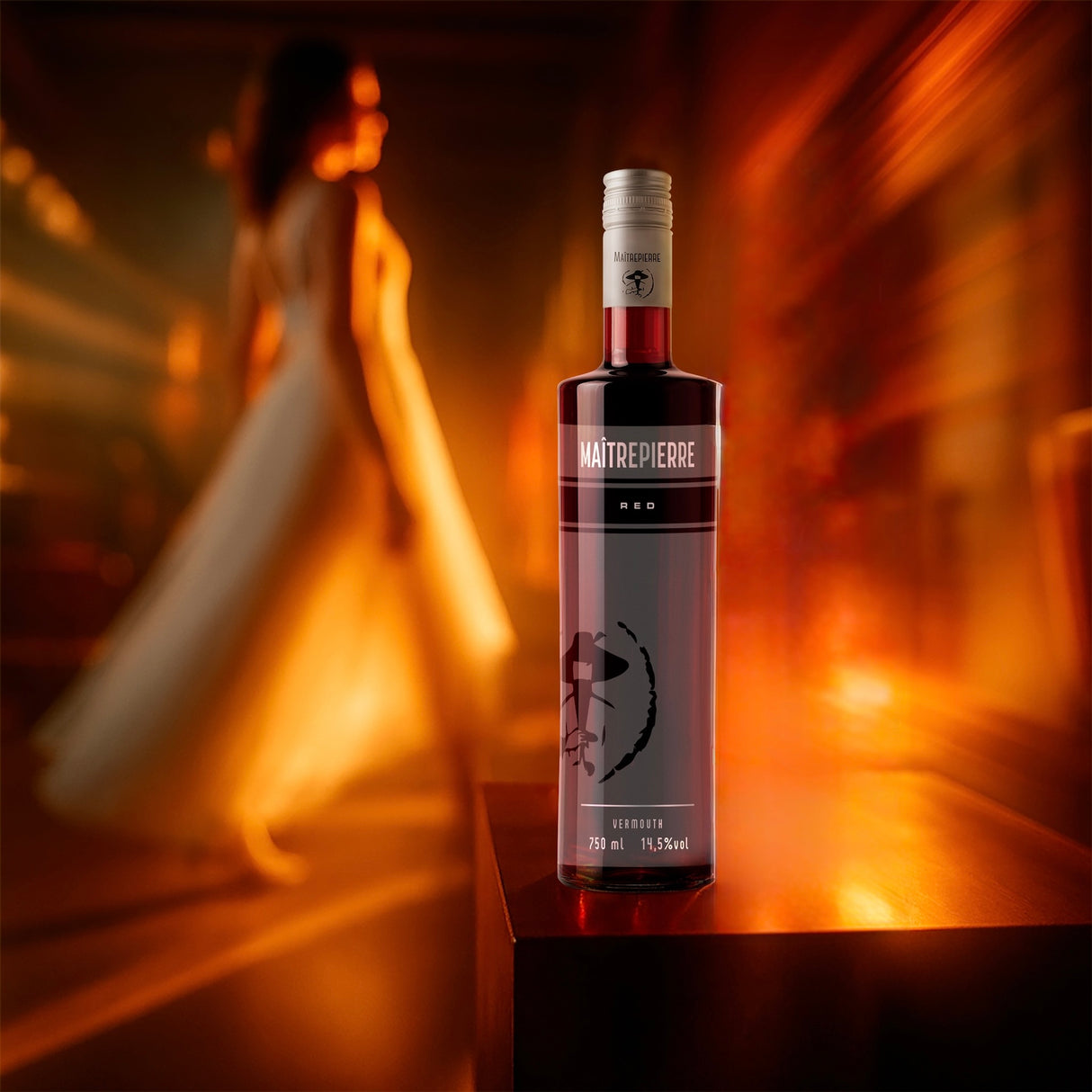 Flasche Maîtrepierre Rouge Wermut auf Tisch im Vordergrund, im Hintergrund verschwommene Frau im weißen Kleid und warmes Licht.