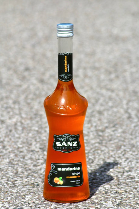 Flasche Mandarinen-Sirup von Sanz in orangener Farbe, mit schwarzem Etikett und silbernem Verschluss auf einer Oberfläche.