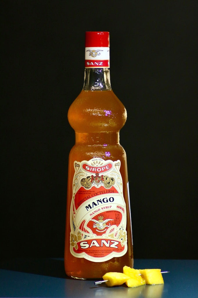 Mango Sirup Sanz 1L Flasche mit verziertem Etikett und frischen Mangostücken auf Spieß