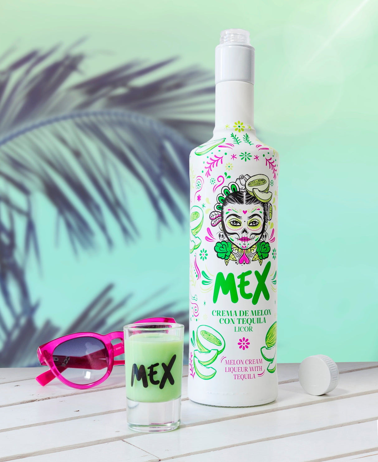 Mex Melonen-Tequila Sahnelikör mit offenem Deckel, grünem Shot im Glas und pinker Sonnenbrille auf weißem Tisch.