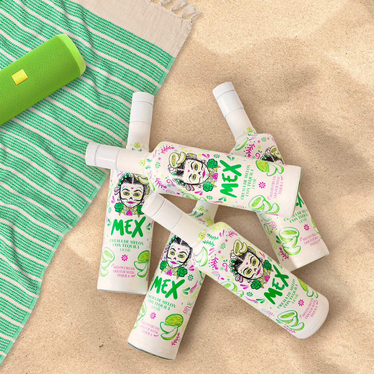 Mex Melonen-Tequila Sahnelikör, vier Flaschen auf Sand mit grün-weißem Handtuch und passendem Lautsprecher.