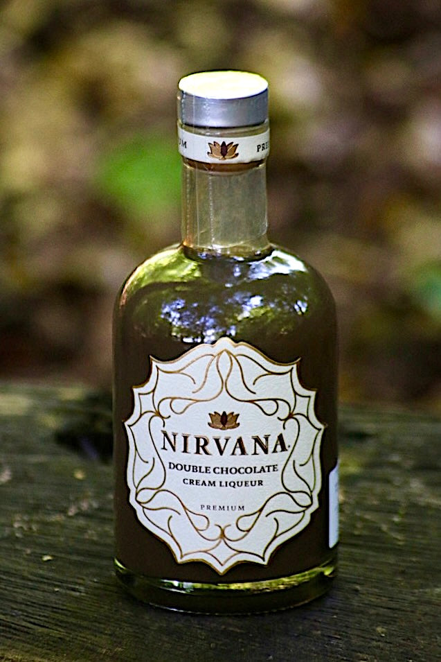 Flasche Nirvana Double Chocolate Cream Liqueur, mit edlem Etikett und dunkler Schokoladenfarbe, auf einem Holztisch vor einem unscharfen, natürlichen Hintergrund.