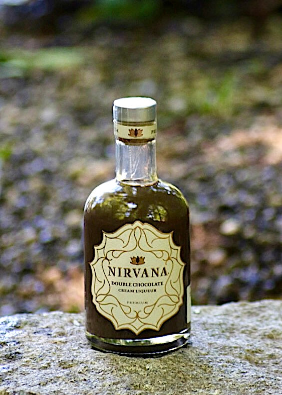 Flasche Nirvana Double Chocolate Cream Liqueur, mit cremefarbenem Etikett und braunem Likör, auf einem Felsen im Freien, vor einem natürlichen, unscharfen Hintergrund.