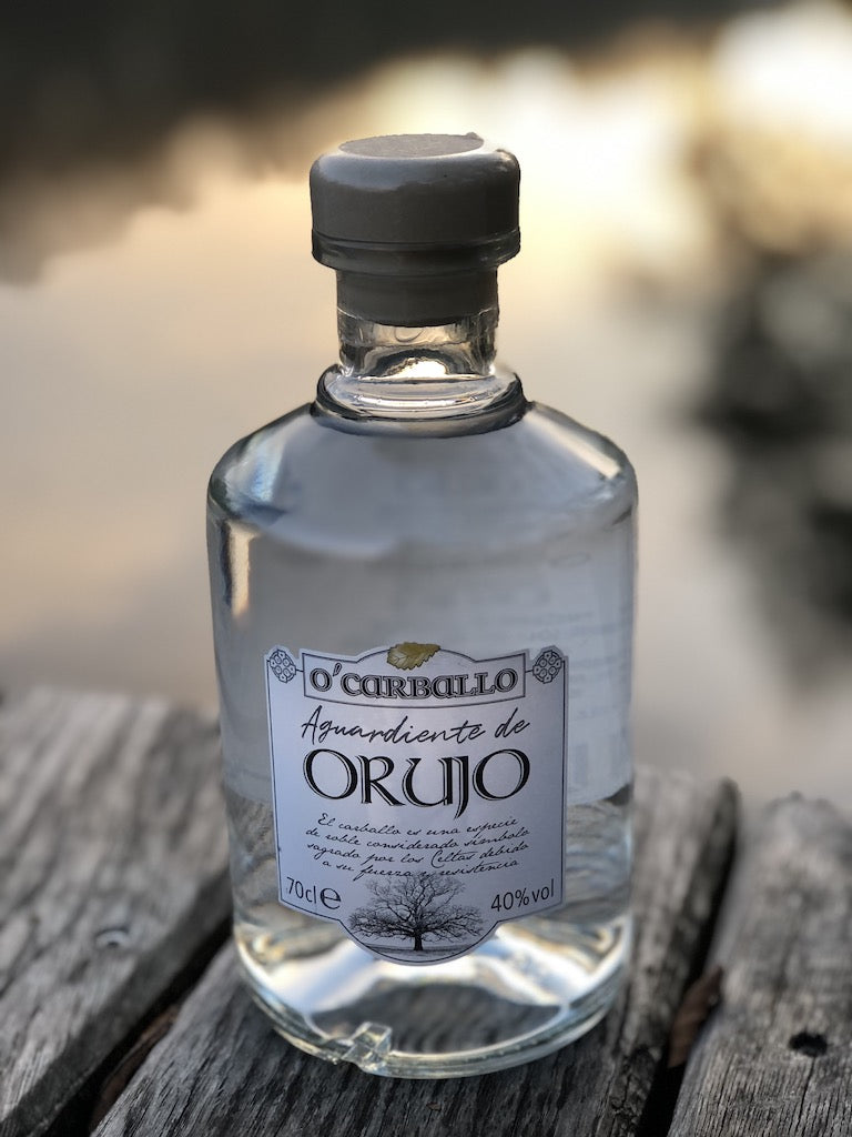 O’Carballo Orujo Flasche auf Holzfläche vor unscharfem Seehintergrund bei Sonnenuntergang, 70 cl, 40 % vol.