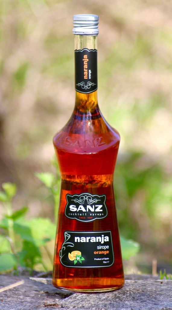 Flasche Sanz Orangensirup auf einem Holzstumpf mit verschwommener Natur im Hintergrund, 70cl.