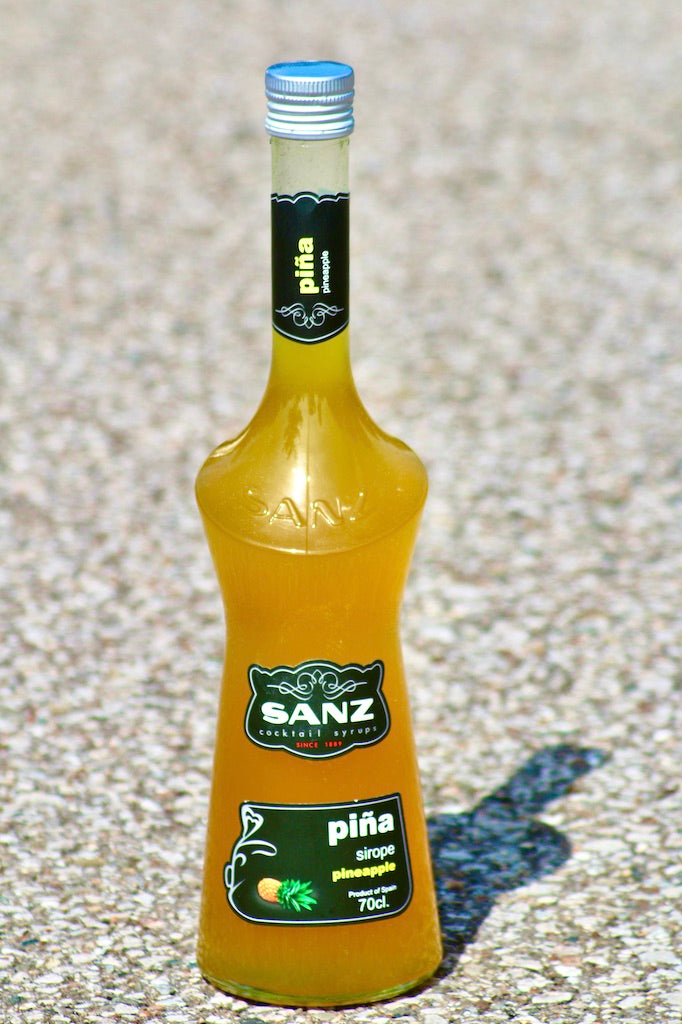 Ananassirup Sanz 0,7L auf hellem Steinboden mit Sonnenlicht und Schatteneffekt.