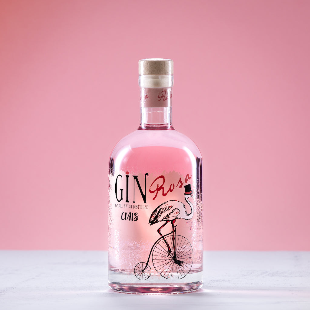Flasche Ciais Gin Rosa von Bordiga mit rosa Inhalt und Flamingo-Design vor rosafarbenem Hintergrund auf hellem Untergrund.