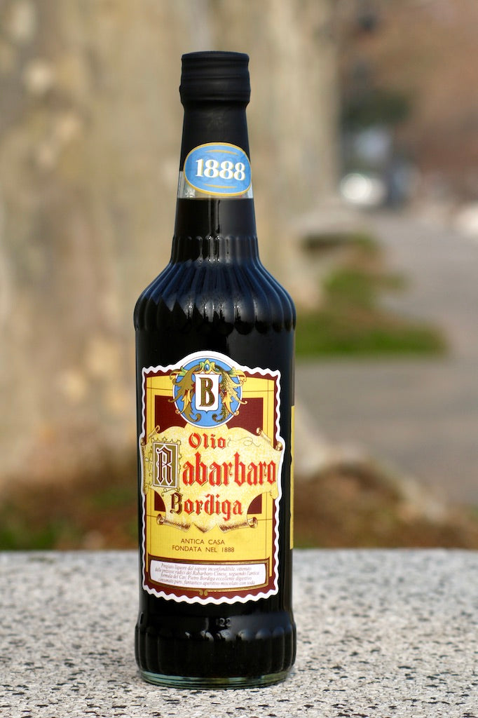 Flasche Olio di Rabarbaro Bordiga Rhabarber-Likör mit dekorativem Etikett, stehend auf Steinoberfläche, unscharfer Hintergrund.