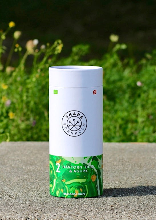 Geschenkbox des Bio-Schnapses von Bornholm, Sanddorn, Dill und Gurke, stehend auf einer Steinoberfläche vor einem unscharfen, grünen Hintergrund.