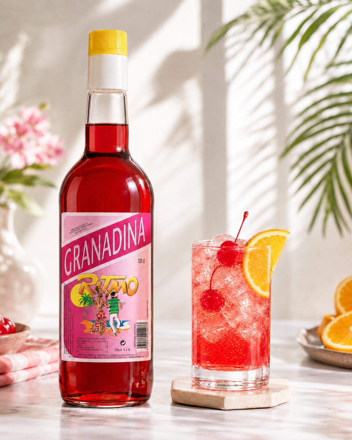 Ritmo Grenadine Flasche neben rotem Shirley Temple mit Eis, Cocktailkirschen und Orangenscheibe.