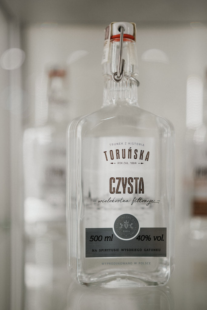 Klare Flasche Toruńska Czysta Wodka 40% vol. mit Bügelverschluss, auf einem Regal oder in einem Display präsentiert.