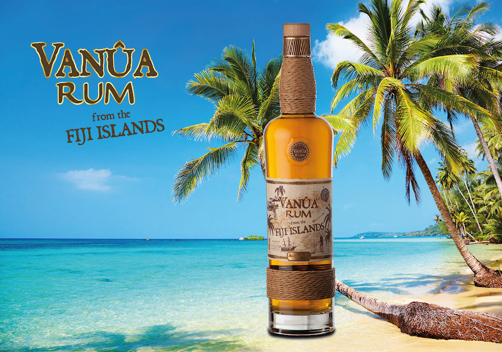Flasche Vanua Rum Añejo vor tropischer Strandkulisse mit Palmen und türkisblauem Meer, Fiji-Inseln, 3-5 Jahre gereift.