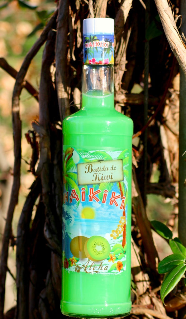 Flasche Batida de Kiwi Waikiki Likör mit tropischem Etikett, vor einem Hintergrund aus Ästen und Blättern