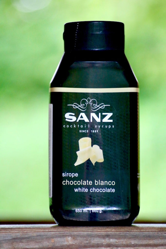 Weiße Schokolade Sirup Sanz in einer schwarzen 650-ml-Flasche mit weißem Etikett auf Holzoberfläche.
