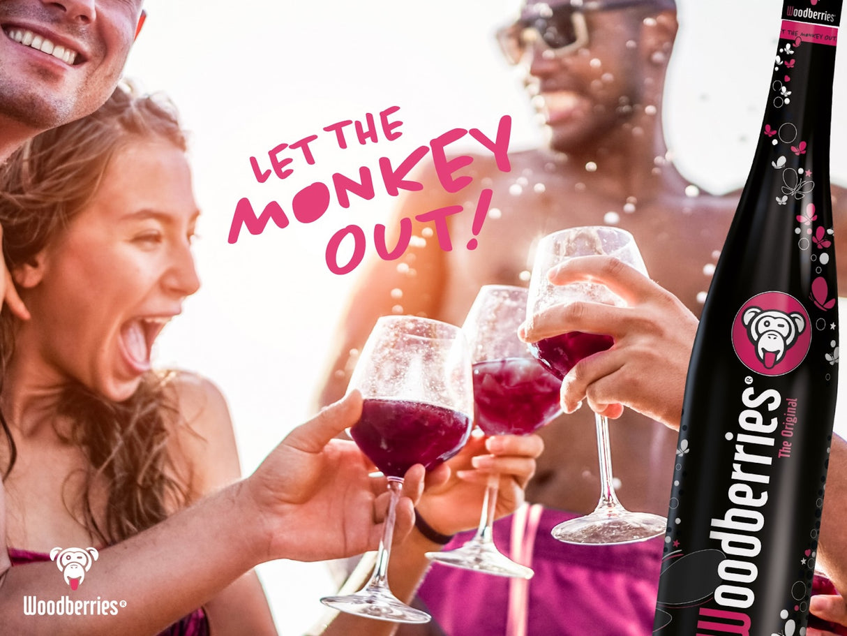 Menschen feiern am Strand mit Gläsern Woodberries Aperitif, daneben Flasche und Schriftzug „Let the Monkey out!“.