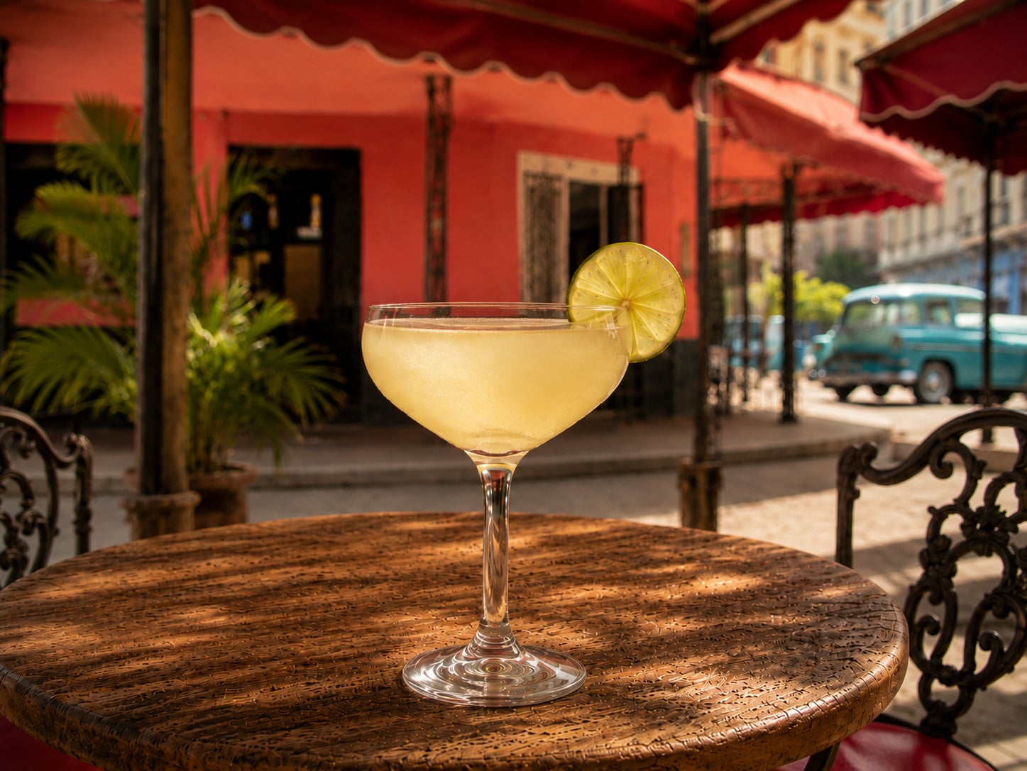 Daiquiri-Cocktail mit Limettenscheibe auf Holztisch vor kubanischer Straßenszene mit Oldtimer